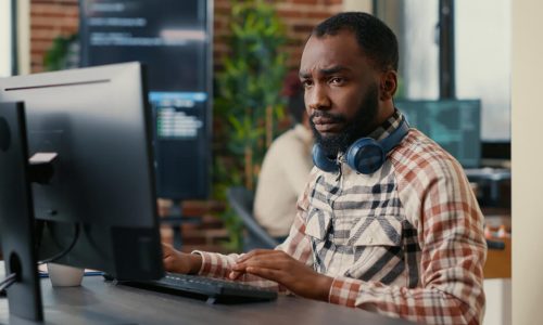 portrait-focused-african-american-programer-wearing-wireless-headphones-working-looking-computer-screen-while-typing-software-developer-writing-code-it-agency-office (1)